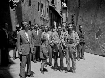 Movie still from “Bicycle Thieves” (1948), directed by Vittorio De Sica – Black and white photograph of a group of men standing on a street; Wide shot, Low angle