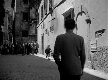 Movie still from “Bicycle Thieves” (1948), directed by Vittorio De Sica – A man standing in front of a group of people on a street; Wide shot, Over the shoulder angle