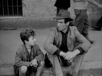 Movie still from “Bicycle Thieves” (1948), directed by Vittorio De Sica – A man sitting next to a young boy on the ground; Medium shot, High angle