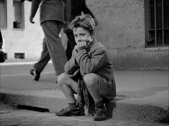 Movie still from “Bicycle Thieves” (1948), directed by Vittorio De Sica – A young boy sitting on the steps of a building; Medium shot, High angle