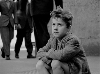 Movie still from “Bicycle Thieves” (1948), directed by Vittorio De Sica – A young boy sitting on the ground in front of a group of people; Medium shot, High angle