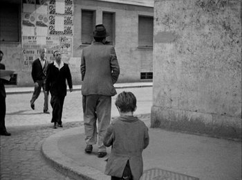 Movie still from “Bicycle Thieves” (1948), directed by Vittorio De Sica – A man and a child walking down a street; Wide shot, Over the shoulder angle