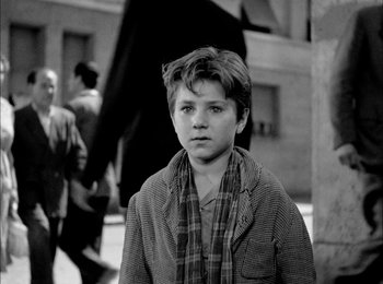 Movie still from “Bicycle Thieves” (1948), directed by Vittorio De Sica – A young boy wearing a plaid jacket and a scarf; Medium shot, Over the shoulder angle