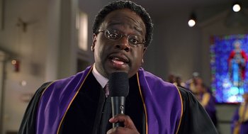 Movie still from “Big Momma's House” (2000), directed by Raja Gosnell – A man in a purple and black robe holding a microphone; Close Up shot, Low angle
