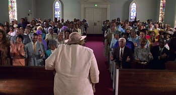 Movie still from “Big Momma's House” (2000), directed by Raja Gosnell – An older woman wearing a hat and a long coat walks in front of a crowd; Wide shot, Low angle