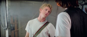 Movie still from “Bill & Ted's Excellent Adventure” (1989), directed by Stephen Herek – A young man with blonde curly hair wearing a white t - shirt; Close Up shot, Over the shoulder angle