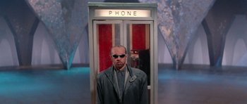 Movie still from “Bill & Ted's Excellent Adventure” (1989), directed by Stephen Herek – A man standing in front of a phone booth wearing sunglasses; Wide shot, Low angle