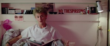 Movie still from “Bill & Ted's Excellent Adventure” (1989), directed by Stephen Herek – A man sitting on a chair reading a book in a room; Medium shot, Over the shoulder angle