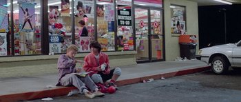 Movie still from “Bill & Ted's Excellent Adventure” (1989), directed by Stephen Herek – A couple of people sitting on the ground outside of a store; Wide shot, High angle