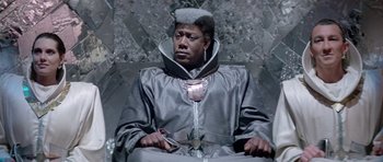 Movie still from “Bill & Ted's Excellent Adventure” (1989), directed by Stephen Herek – A man sitting in a chair wearing a suit and holding a cell phone; Medium shot, Low angle