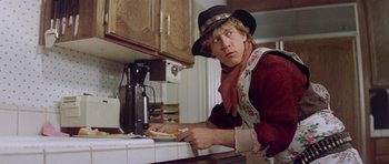 Movie still from “Bill & Ted's Excellent Adventure” (1989), directed by Stephen Herek – A man wearing a hat and scarf leaning over a counter; Medium shot, Low angle