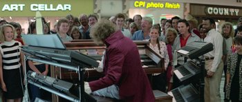 Movie still from “Bill & Ted's Excellent Adventure” (1989), directed by Stephen Herek – A woman is playing the piano in front of a group of people; Wide shot, Over the shoulder angle