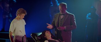 Movie still from “Bill & Ted's Excellent Adventure” (1989), directed by Stephen Herek – A man in a suit and a tie standing next to a woman in a chair; Medium shot, Over the shoulder angle