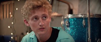 Movie still from “Bill & Ted's Excellent Adventure” (1989), directed by Stephen Herek – A man with curly blonde hair sitting in front of a glass; Close Up shot, Low angle