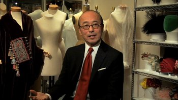 A man sitting in front of mannequins wearing a suit and red tie