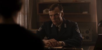 Movie still from “Dark” (2017), created by Baran bo Odar – A man in uniform sitting in front of a table; Medium shot, Over the shoulder angle