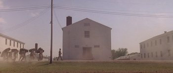 Movie still from “Biloxi Blues” (1988), directed by Mike Nichols – A person walking in front of a white building; Extreme Wide shot, Low angle