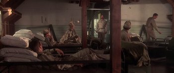 Movie still from “Biloxi Blues” (1988), directed by Mike Nichols – A group of men sitting on a bed in front of a mirror; Wide shot, High angle