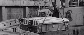 Movie still from “Biloxi Blues” (1988), directed by Mike Nichols – A black and white photo of a man standing next to an american flag bed; Wide shot, High angle