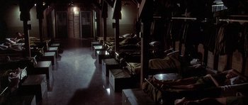 Movie still from “Biloxi Blues” (1988), directed by Mike Nichols – A row of beds in a dark room with lights on; Wide shot, High angle