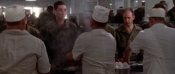 Movie still from “Biloxi Blues” (1988), directed by Mike Nichols – A group of men standing in a kitchen preparing food; Medium shot, Over the shoulder angle