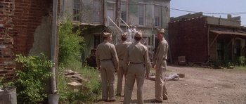 Movie still from “Biloxi Blues” (1988), directed by Mike Nichols – A group of men standing next to each other in front of a building; Wide shot, Low angle
