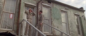 Movie still from “Biloxi Blues” (1988), directed by Mike Nichols – Two young men standing on the steps of an old building saluting each other; Wide shot, Low angle