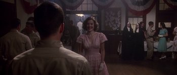 Movie still from “Biloxi Blues” (1988), directed by Mike Nichols – A woman in a pink dress standing next to a man in a suit; Medium shot, Over the shoulder angle