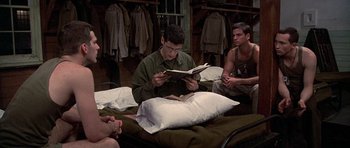 Movie still from “Biloxi Blues” (1988), directed by Mike Nichols – A man sitting on a bed reading a book; Medium shot, High angle