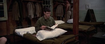 Movie still from “Biloxi Blues” (1988), directed by Mike Nichols – A man sitting on a bed reading a book; Wide shot, High angle