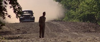 Movie still from “Biloxi Blues” (1988), directed by Mike Nichols – A man standing on the side of a road near a car; Wide shot, Low angle