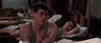 Movie still from “Biloxi Blues” (1988), directed by Mike Nichols – A man sitting on top of a bed next to another man; Medium shot, Over the shoulder angle