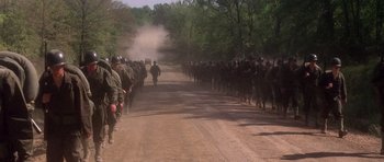Movie still from “Biloxi Blues” (1988), directed by Mike Nichols – A large group of soldiers marching down a dirt road; Extreme Wide shot, High angle