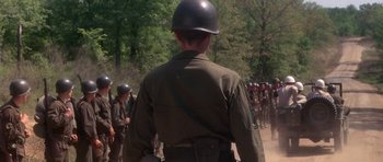 Movie still from “Biloxi Blues” (1988), directed by Mike Nichols – A man in a helmet is standing in front of a group of soldiers; Medium shot, Over the shoulder angle