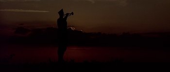 Movie still from “Biloxi Blues” (1988), directed by Mike Nichols – A man playing a trumpet in a field at night; Extreme Wide shot, Low angle