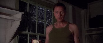 Movie still from “Biloxi Blues” (1988), directed by Mike Nichols – A man standing in front of a window at night holding a remote control; Medium shot, Low angle