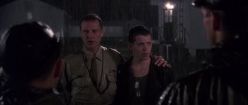 Movie still from “Biloxi Blues” (1988), directed by Mike Nichols – Two men standing in the rain with one holding a cigarette in his mouth; Medium shot, Over the shoulder angle