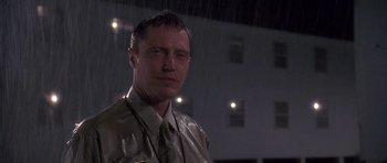 Movie still from “Biloxi Blues” (1988), directed by Mike Nichols – A man standing in front of a building in the rain; Close Up shot, Low angle