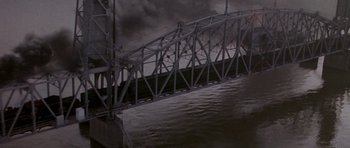 Movie still from “Biloxi Blues” (1988), directed by Mike Nichols – A bridge that is over a body of water under a cloudy sky; Extreme Wide shot, High angle
