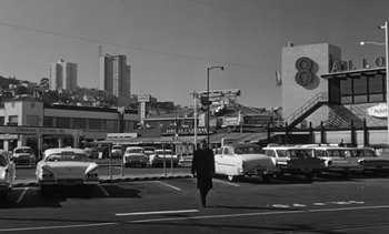 Movie still from “Birdman of Alcatraz” (1962), directed by John Frankenheimer – A person walking across a street near a lot of cars; Wide shot, Low angle