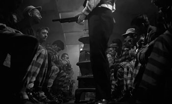 Movie still from “Birdman of Alcatraz” (1962), directed by John Frankenheimer – A group of men sitting in a room with a man holding a gun; Wide shot, Low angle