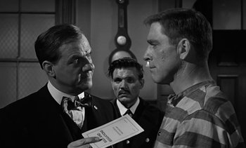 Movie still from “Birdman of Alcatraz” (1962), directed by John Frankenheimer – Two men in suits and one man in a tie is holding a piece of paper; Medium shot, Over the shoulder angle
