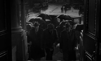 Movie still from “Birdman of Alcatraz” (1962), directed by John Frankenheimer – A group of men walking down a street holding umbrellas; Wide shot, High angle