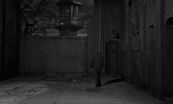 Movie still from “Birdman of Alcatraz” (1962), directed by John Frankenheimer – A man standing on the sidewalk in front of a building; Extreme Wide shot, High angle