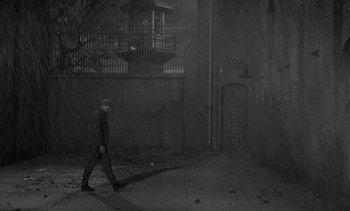 Movie still from “Birdman of Alcatraz” (1962), directed by John Frankenheimer – A man is walking in the rain on the sidewalk; Extreme Wide shot, High angle