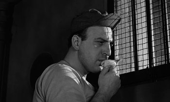 A black and white photo of a man smoking a cigarette in front of a window