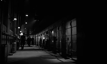 Movie still from “Birdman of Alcatraz” (1962), directed by John Frankenheimer – People walking down a dark hallway in a jail cell at night; Extreme Wide shot, High angle