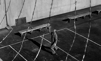 Movie still from “Birdman of Alcatraz” (1962), directed by John Frankenheimer – A man walking across a tennis court holding a racquet; Wide shot, High angle