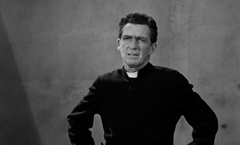 Movie still from “Birdman of Alcatraz” (1962), directed by John Frankenheimer – A man wearing a priest's outfit with his hands on his hips; Medium shot, High angle