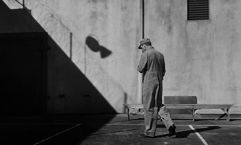 Movie still from “Birdman of Alcatraz” (1962), directed by John Frankenheimer – An older man walking down a sidewalk in front of a building; Wide shot, Low angle